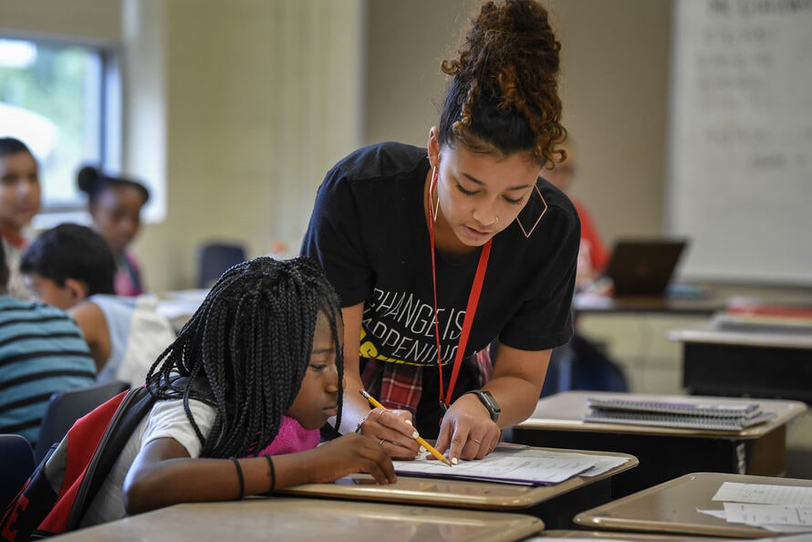 A Teach For America corps member working with a young student at her desk.